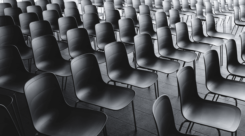 Plan rapproché montrant des chaises en plastique noir alignées sur plusieurs rangées.